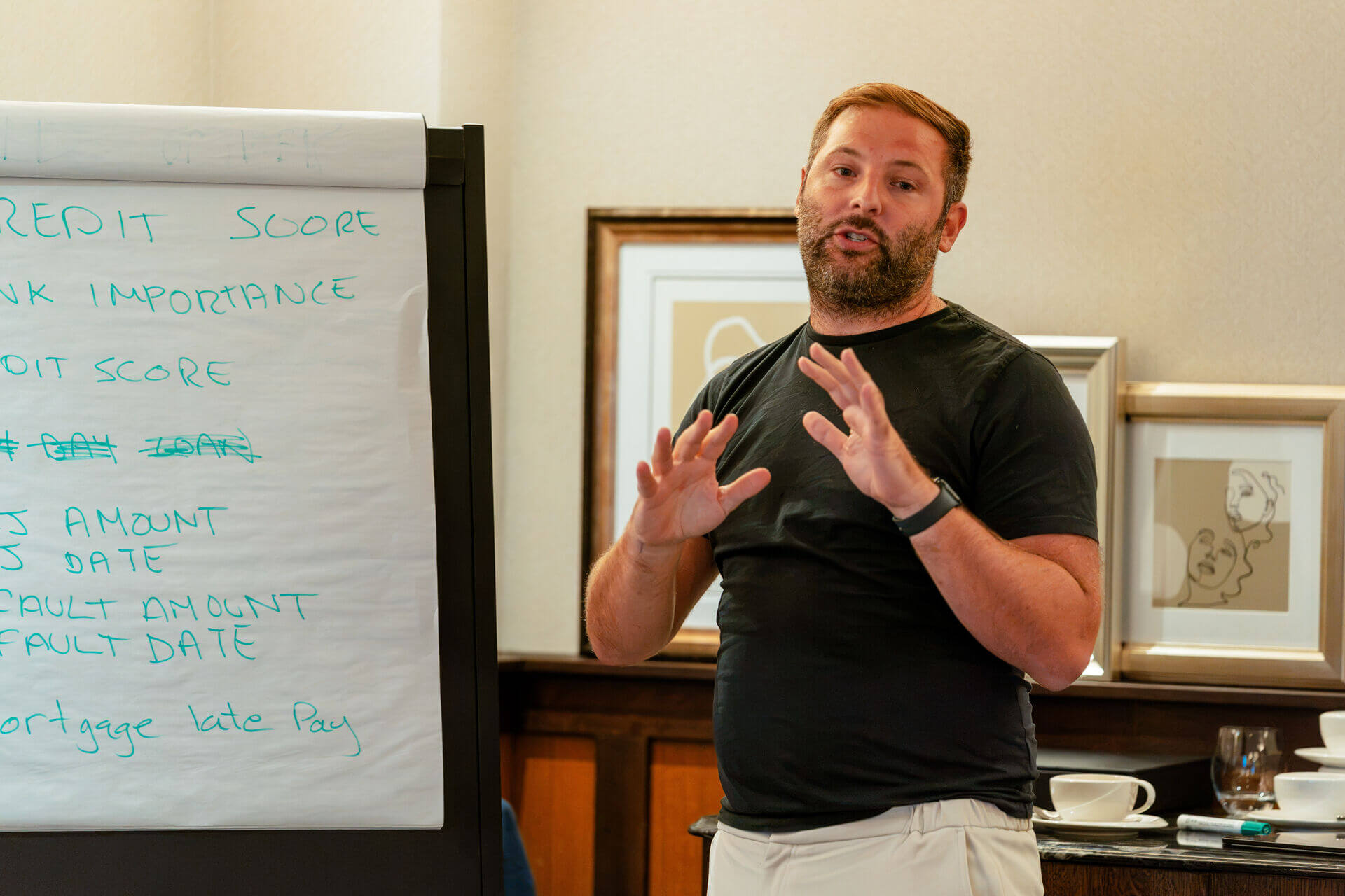 A man gestures while presenting beside a flip chart covered with handwritten notes.
