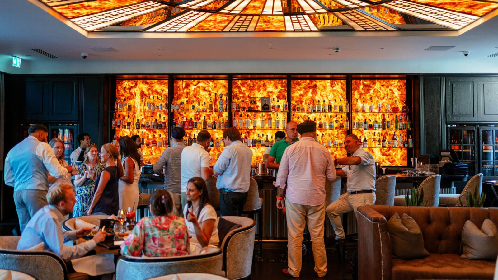 Guests mingle in an elegant lounge in front of a brightly illuminated bar.